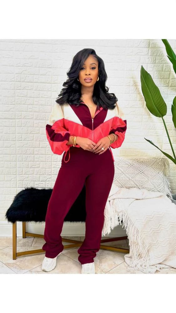 A woman wearing a red and white color-blocked zip-up tracksuit with matching maroon pants and white sneakers, standing against a neutral background.