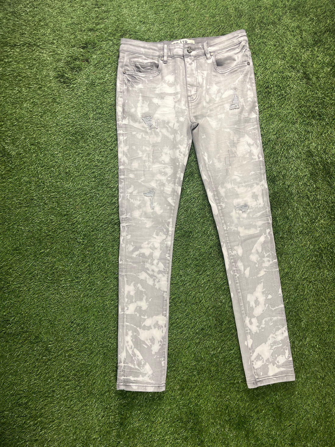 Light grey distressed jeans with a marbled pattern, featuring rips and a slim fit design.