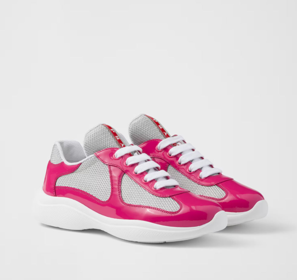 Pair of Prada sneakers with glossy hot pink overlays, white laces, grey mesh panels, and chunky white rubber soles on white background.