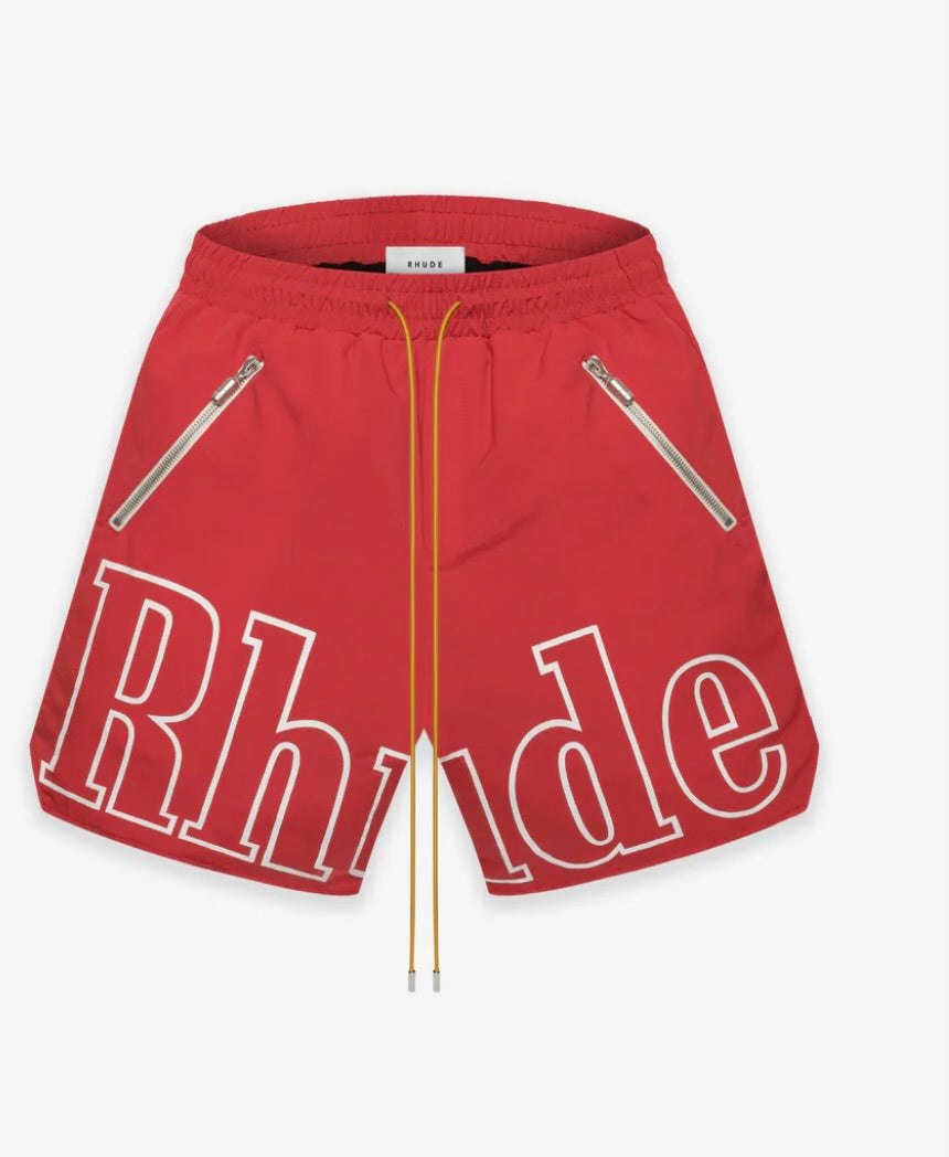 Red Rhude shorts with bold white outlined logo text across the front, featuring yellow drawstrings and two diagonal zippered pockets.