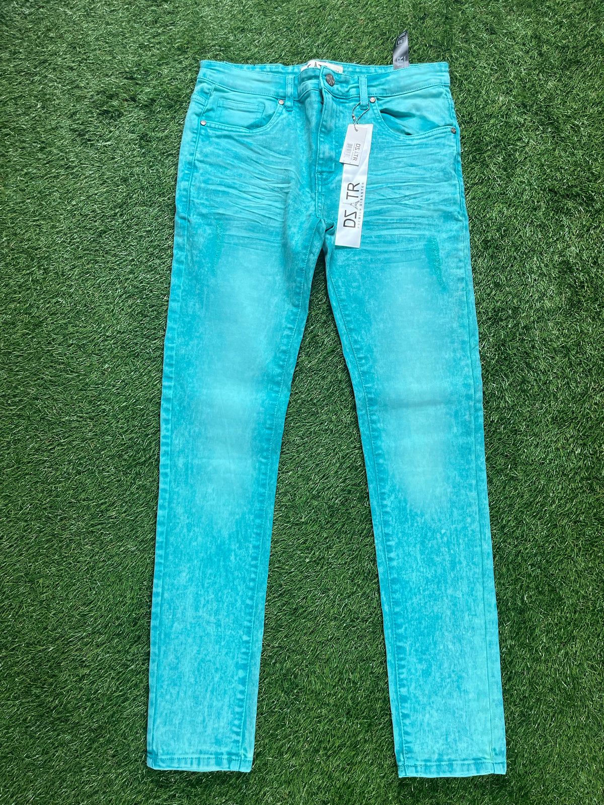 A pair of bright turquoise skinny jeans with a faded look, hanging with price tags still attached.