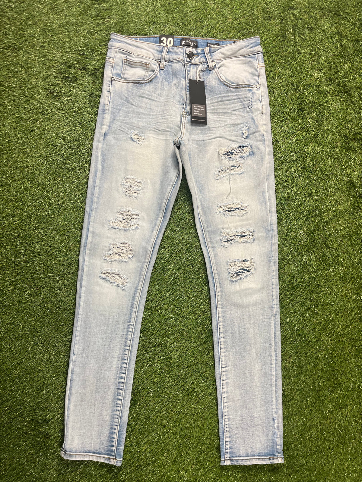 A pair of light-wash ripped skinny jeans with distressed details on the front, featuring a tag attached to the waistband.