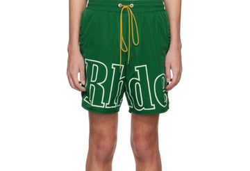Man wearing green Rhude shorts with large white logo text across the front and yellow drawstring, standing with arms by sides.
