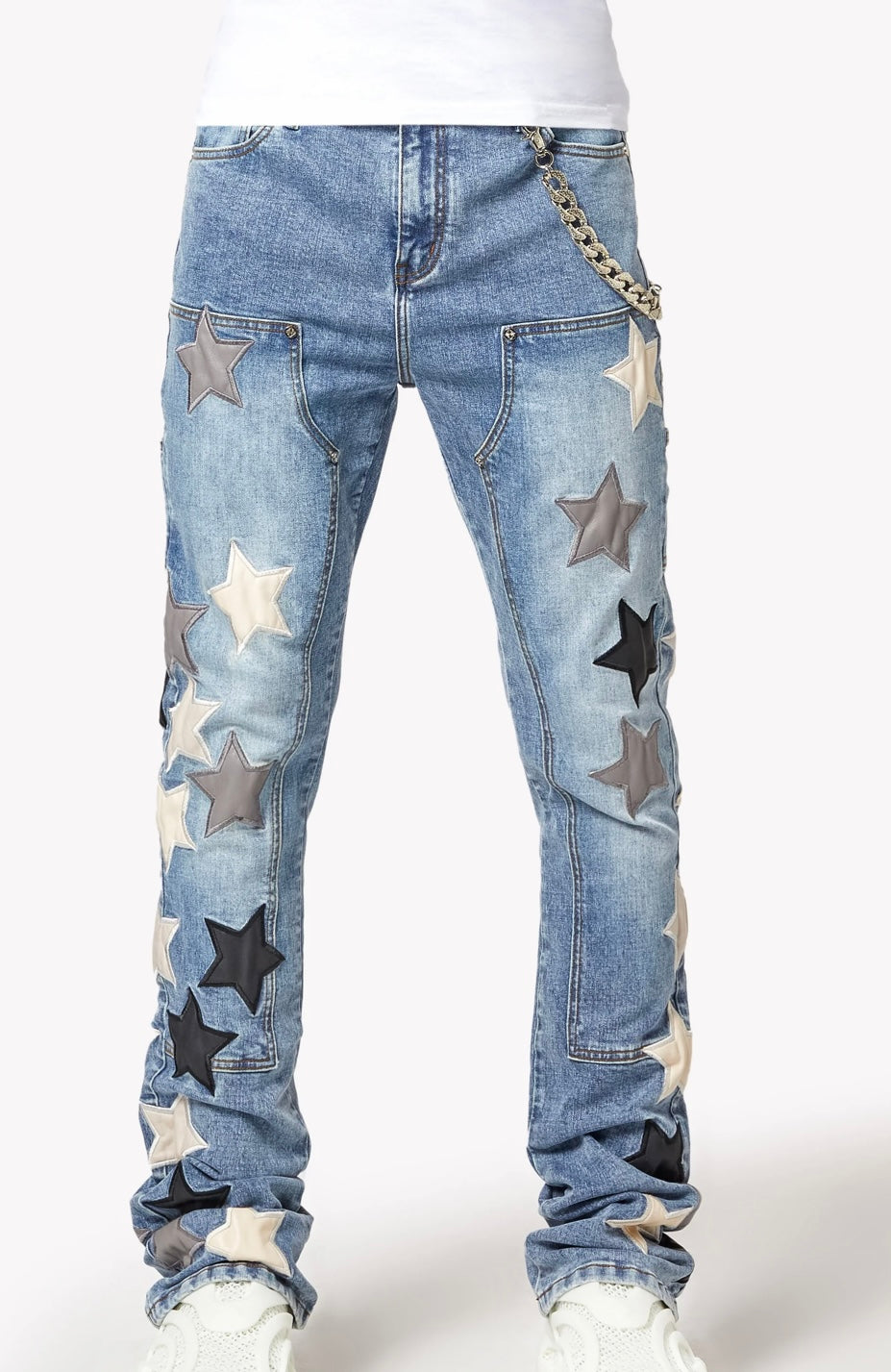 Light blue jeans featuring large multi-colored star patches in grey, black, and white, paired with white sneakers and a chain.