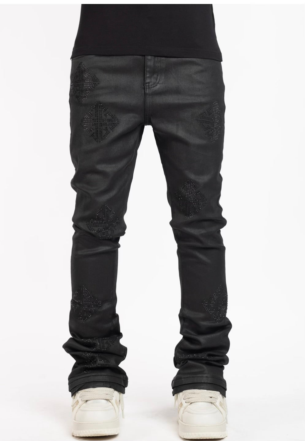A pair of black leather jeans featuring studded diamond-shaped designs on the thighs and paired with white sneakers.
