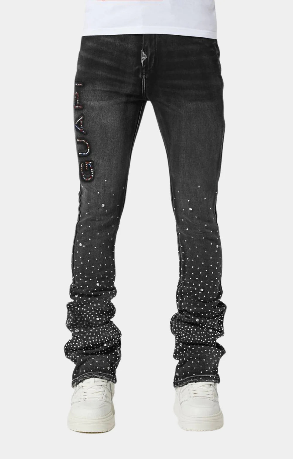 Black jeans with rhinestone embellishments, featuring a “GUAP” design on the left thigh and a slim, stacked fit. Paired with white sneakers.