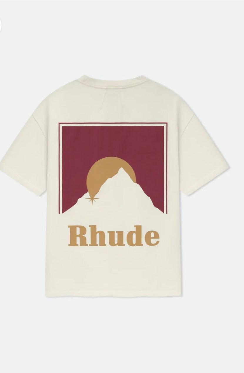 A beige Rhude t-shirt with a graphic of a mountain, sun, and the brand name "Rhude" in gold on the back.