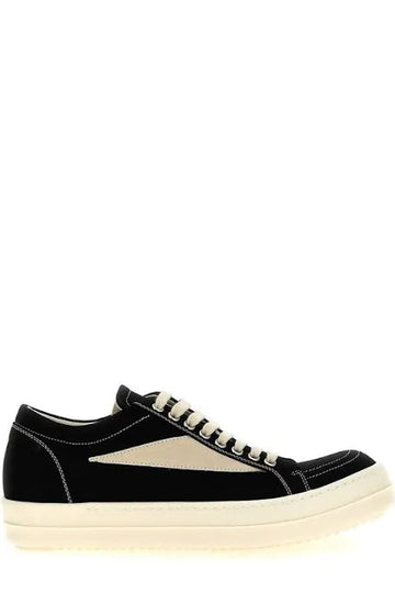 Black sneakers with beige accents and white stitching, featuring a low-profile design and cream-colored sole, displayed from the side.