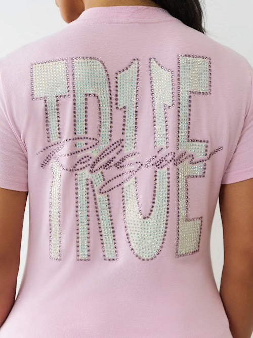 Back view of a woman wearing a pink T-shirt with large rhinestone-studded “TRUE TRUE” text and cursive “Religion” across the back.