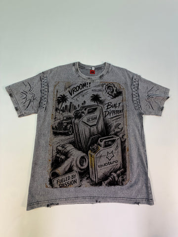 A faded gray graphic t-shirt. The shirt features a distressed, vintage-style black and white illustration of gas cans, a classic car, and palm trees, with text including 'VROOM!', 'BUILT DIFFERENT', and 'FUELED BY PASSION'.