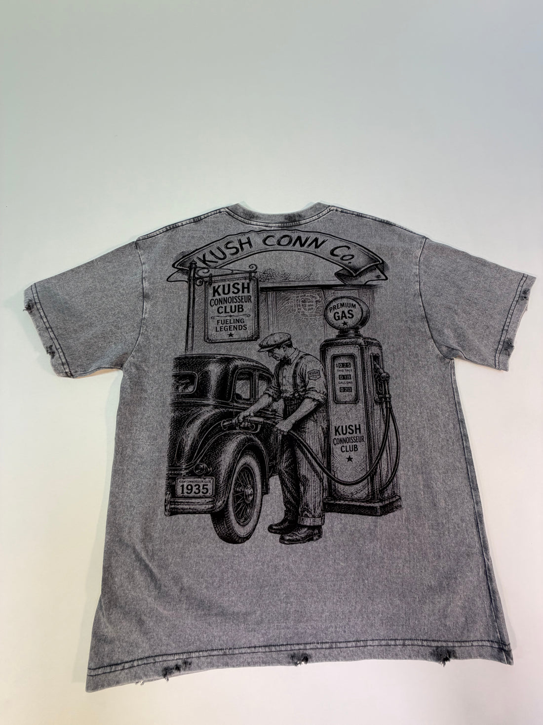 A faded gray graphic t-shirt. The shirt features a distressed, vintage-style black and white illustration of gas cans, a classic car, and palm trees, with text including 'VROOM!', 'BUILT DIFFERENT', and 'FUELED BY PASSION'.